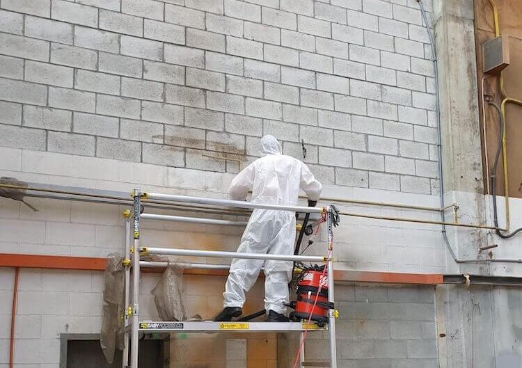 One of PRO ES's Asbestos Removal Experts working on a wall over a scaffolding.