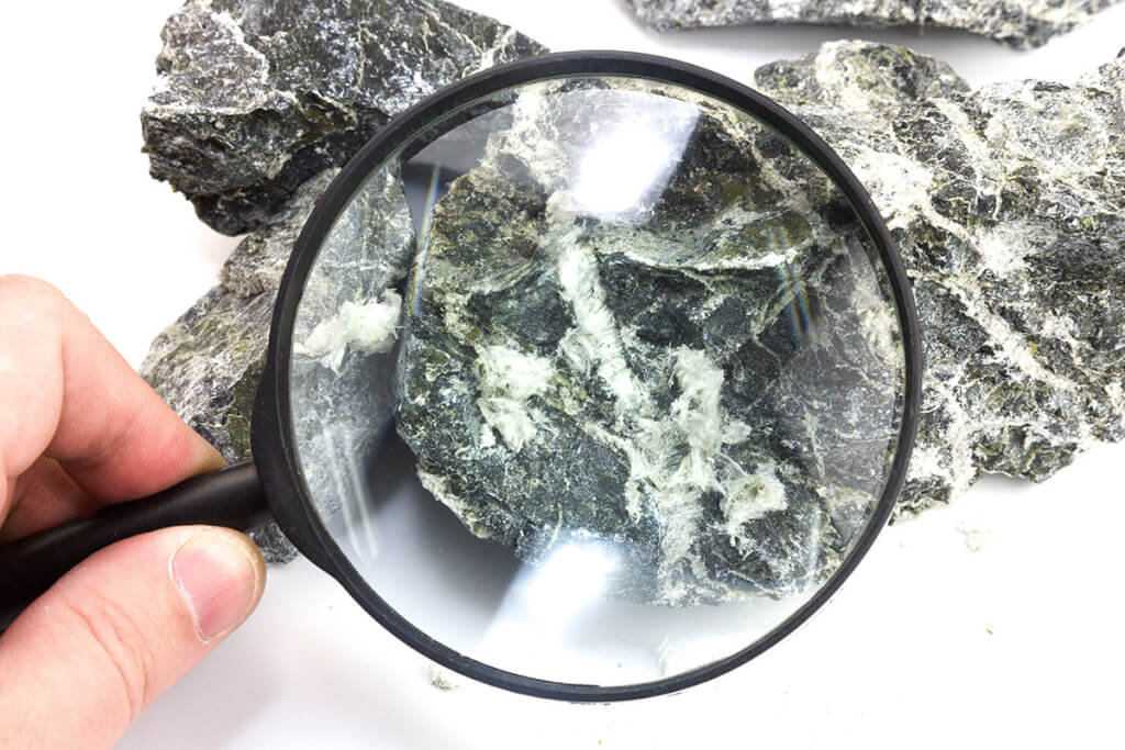 Hand with magnifying glass examines asbestos fibers stone. - class b asbestos products - asbestos removal for demolition and construction sites